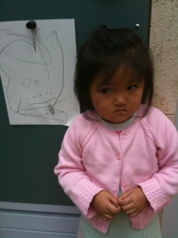 a grumpy toddler standing in front of drawing
